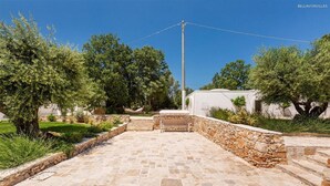 A courtyard with stone flooring, a white building, and trees. - 2410 Tenuta dei Fragni by Perle di Puglia (Ostuni)
