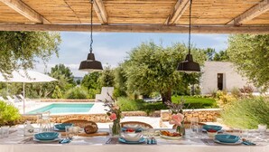 An outdoor dining area with a pool view, wicker chairs, and hanging pendant lights. - 2410 Tenuta dei Fragni by Perle di Puglia (Ostuni)