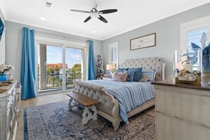 A bedroom with a large bed, a ceiling fan, a view of the outdoors, and a decorative wall piece.