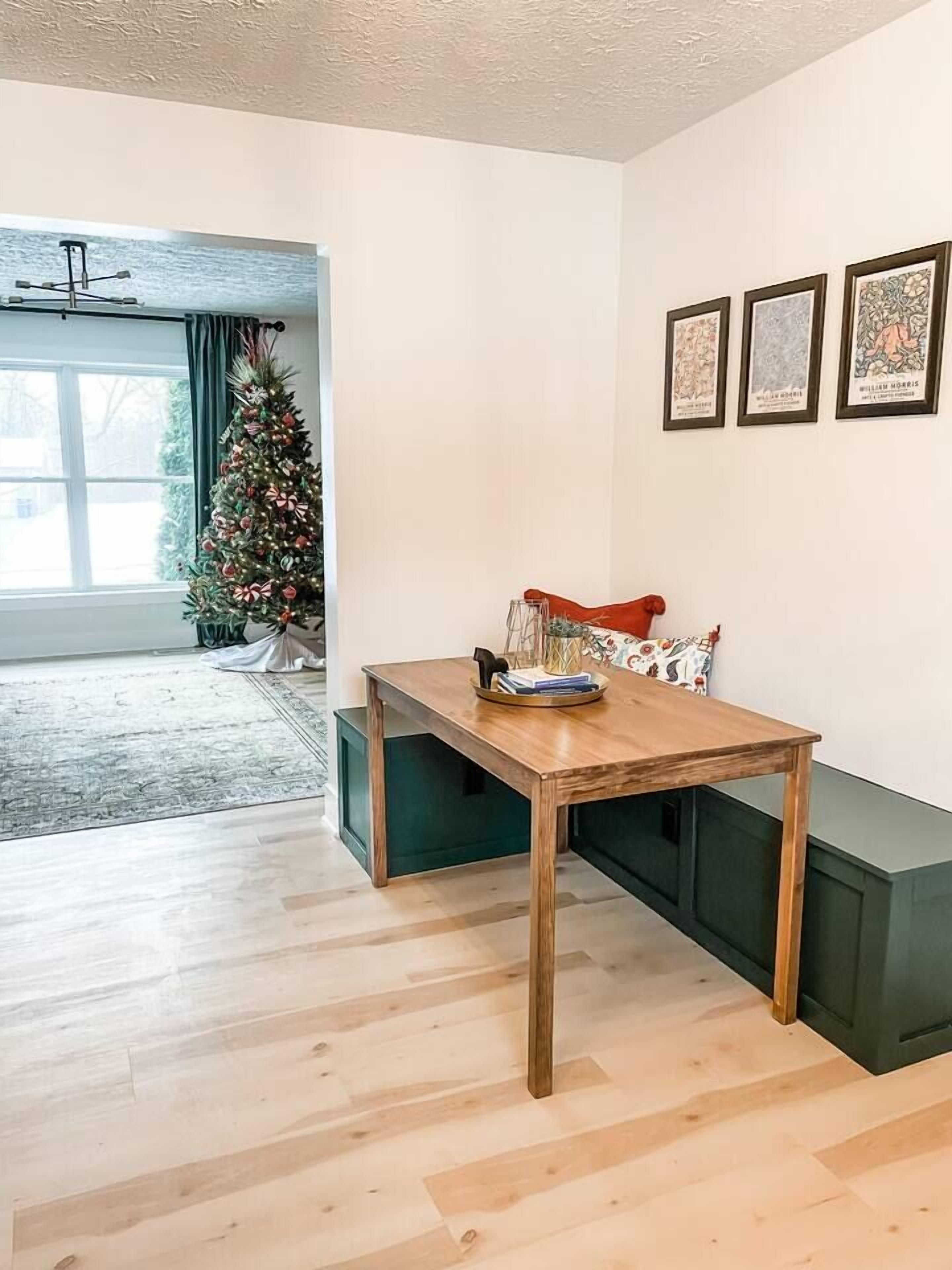 Un comedor con una mesa de madera, un banco y un árbol de Navidad. Hay tres cuadros en la pared.