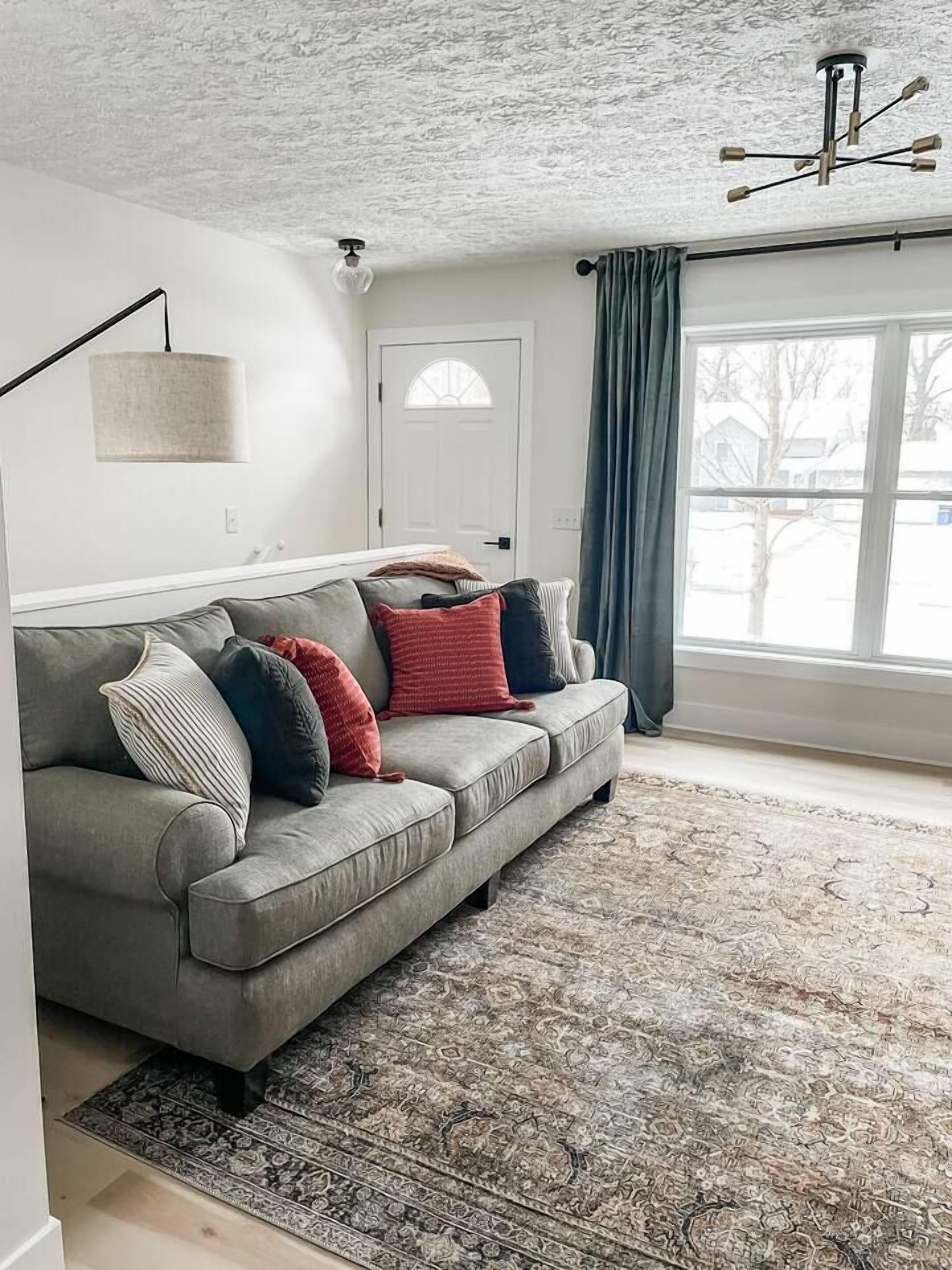 A living room with a grey sofa, patterned rug, and a ceiling light fixture.