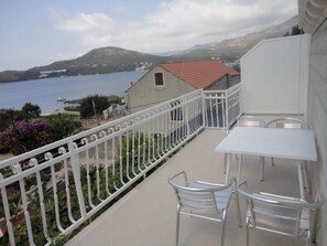 A balcony with a white railing overlooking a body of water and hills. There are two white tables and two chairs. - Apartments Marija Slano- Two-bedroom Apartment With Balcony and Sea View - 1 (Dubrovacko Primorje)