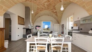 A spacious kitchen with white cabinetry, a dining area with a wooden table and chairs, and a stone arch ceiling. - 777 Rifinita Villa con Piscina a Presicce (Presicce-Acquarica)