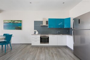 Uma cozinha moderna com armários verde-água, uma geladeira de aço inoxidável e uma área de jantar com cadeiras azuis.