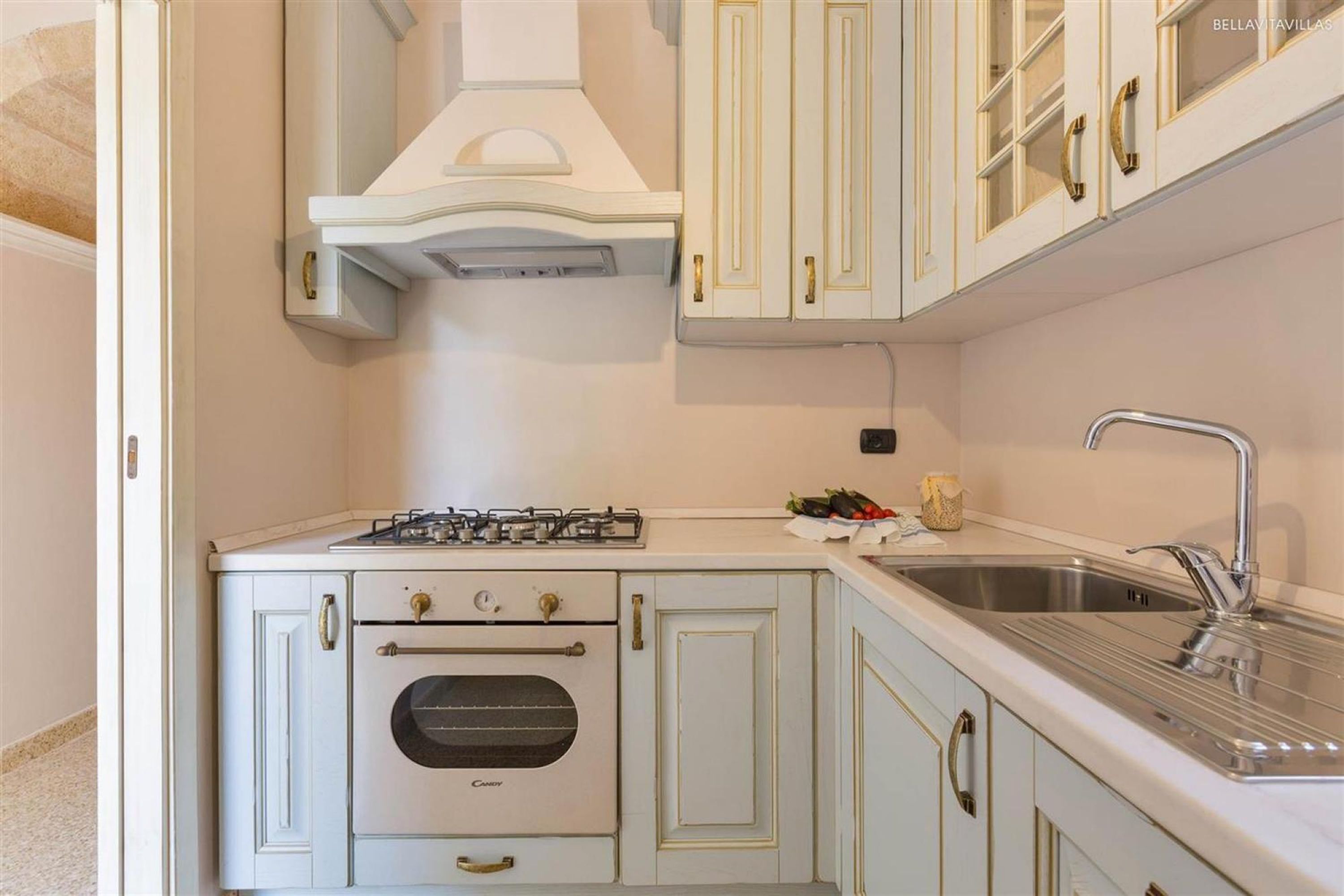 A compact kitchen with white cabinetry, a gas stove, an oven, and a stainless steel sink.