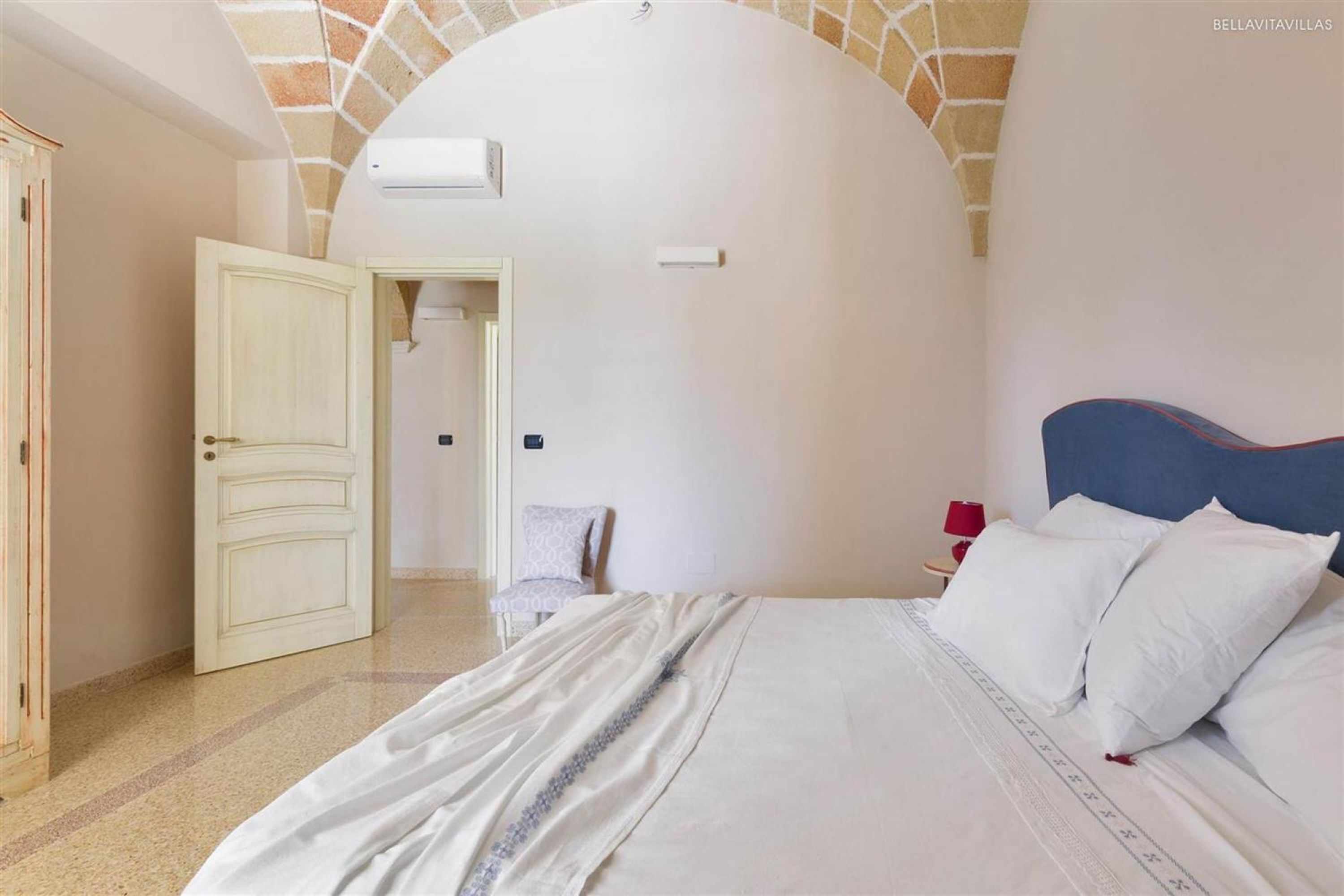 A bedroom with a large bed, a white door, and a red lamp.