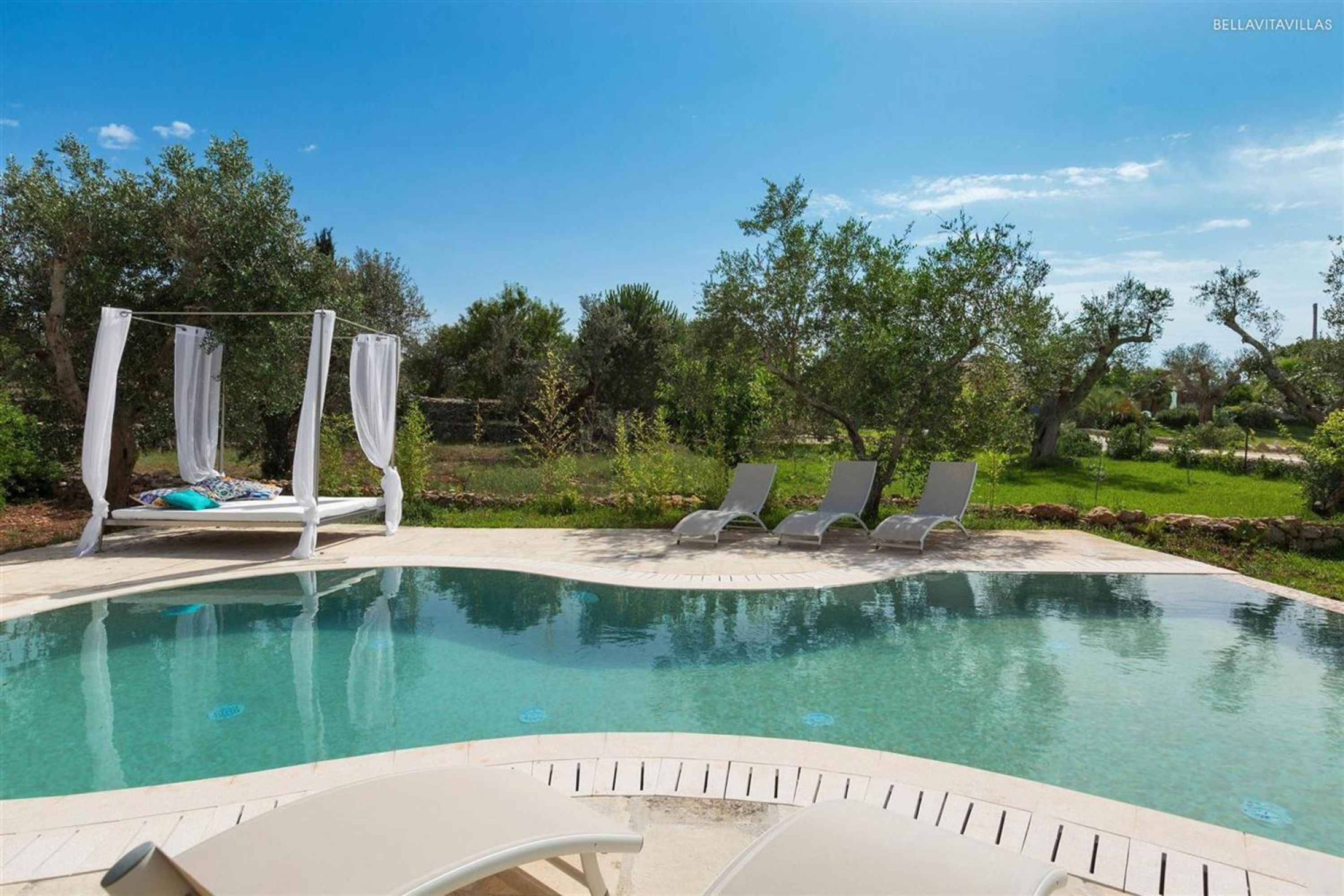 Una piscina con una tenda bianca e poltrone da relax.