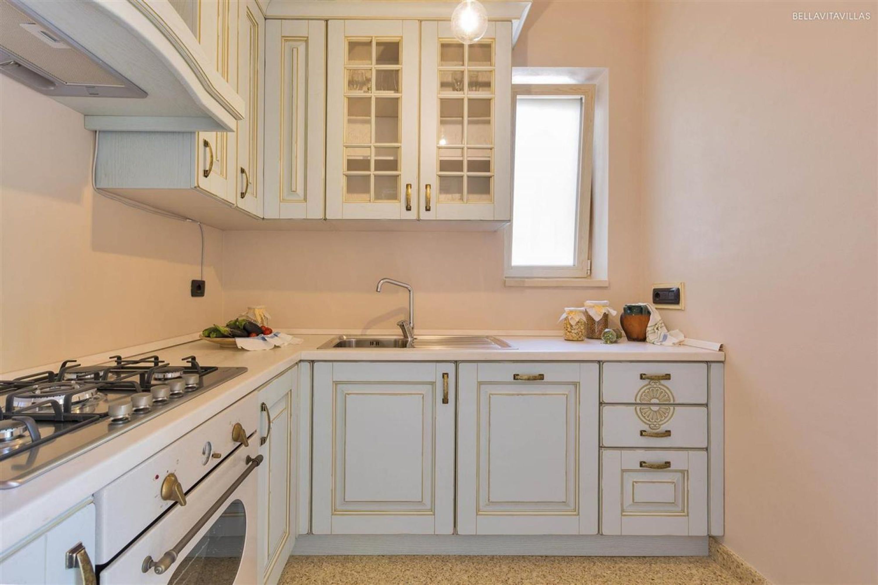 Una cocina con armarios blancos, una estufa a gas y una ventana sobre el lavabo.