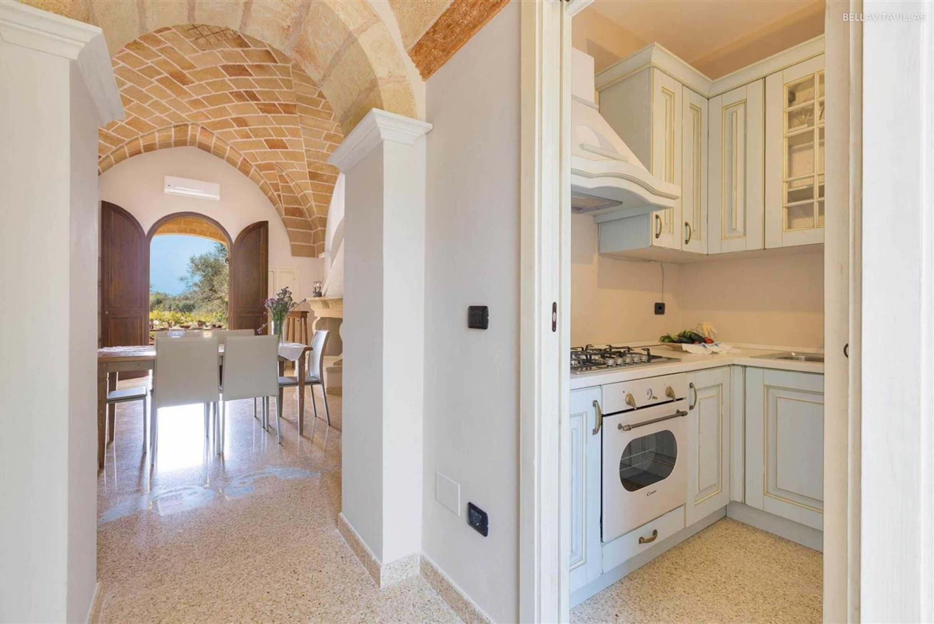 A kitchen with white cabinets, a stove, and an oven. There is a dining area with chairs and a table.