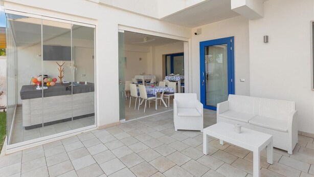 A modern outdoor living area with a glass door leading to a dining space, a white wicker sofa, and a small table. - 1284 B B Dreams and Delights - Comfort Camera Tripla (Porto Cesareo)