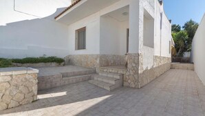 A building with a stone facade, a set of outdoor stairs leading to a covered entrance, and a clear sky. - 1748 Villetta Albachiara (Porto Cesareo)