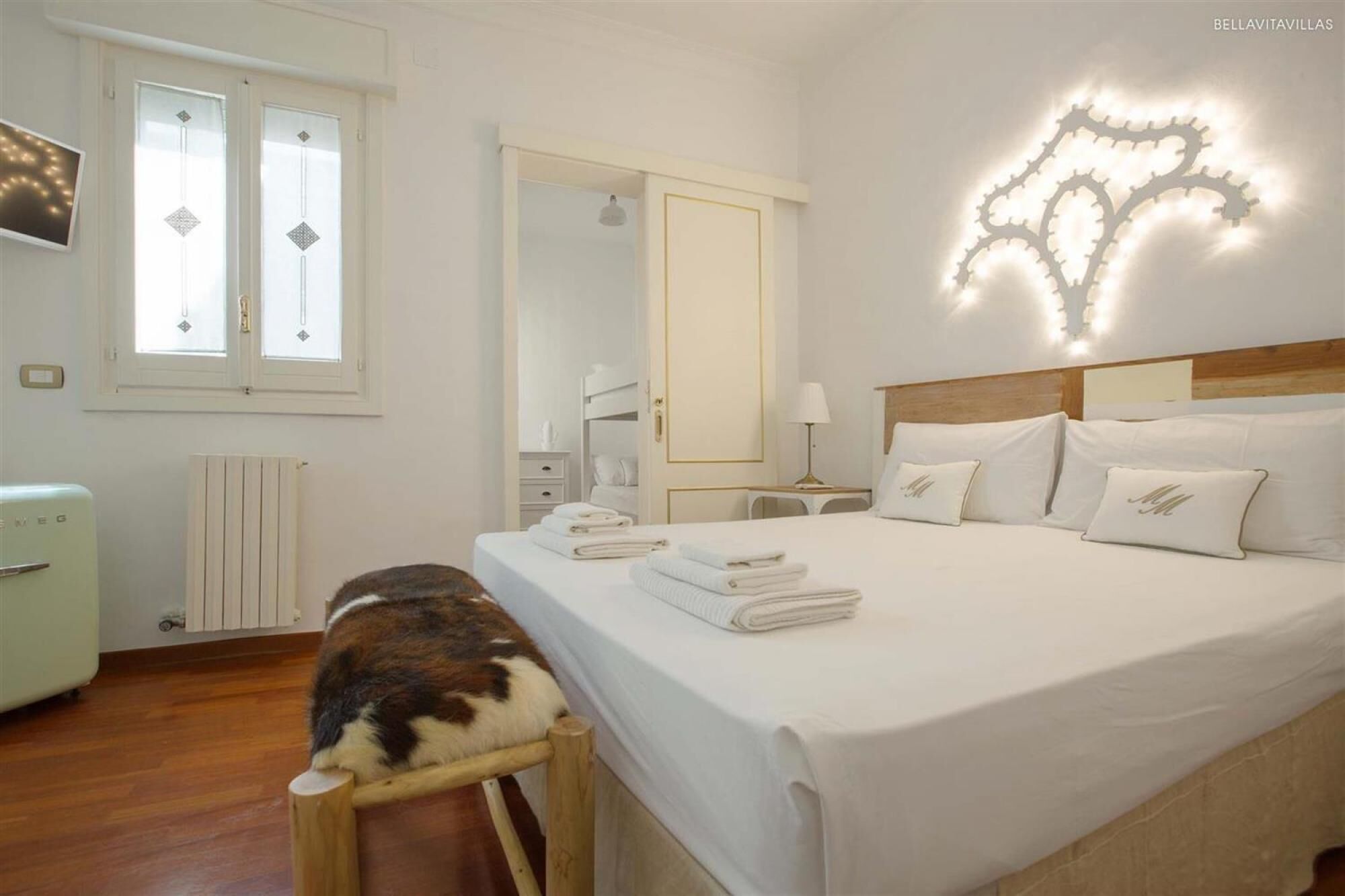 A hotel room with a bed, a chair, a radiator, a window, and a wall-mounted light fixture.