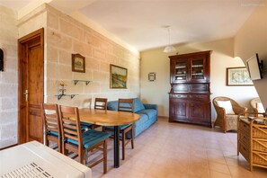 Un espace repas comprenant une table et des chaises en bois, un canapé, des meubles en osier et un mur en pierre.