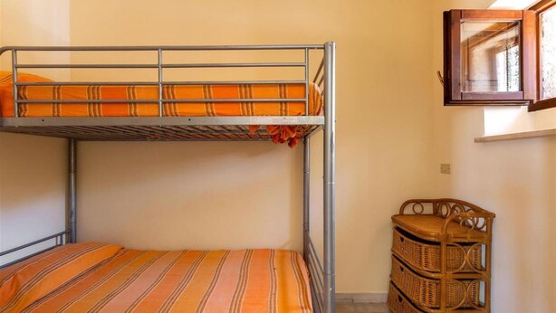 Una cama litera con ropa de cama a rayas, un mueble de almacenamiento de mimbre y una ventana con marco de madera.