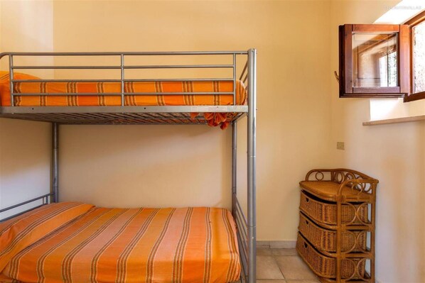 A bunk bed with striped bedding, a wicker storage unit, and a window with a wooden frame.