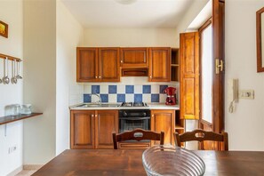 Une cuisine compacte avec des meubles en bois, un pare-feu en carrelage, une cuisinière à gaz, un four et une machine à café.