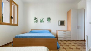 Un dormitorio con una cama de madera, un aparador blanco y un armario. Hay tres cuadros de hojas colgados en la pared.
