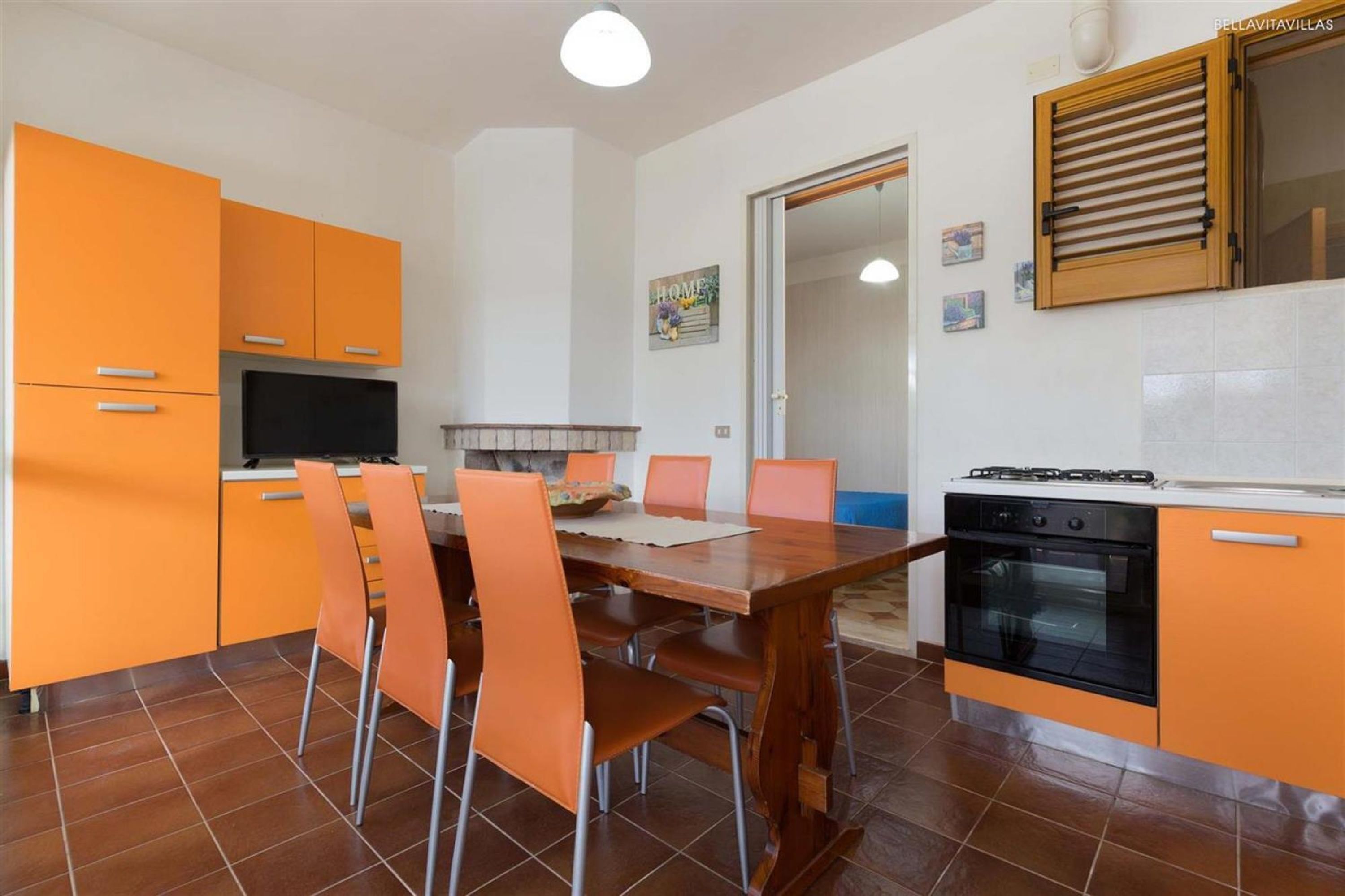 Una cocina compacta con armarios color naranja, una mesa de comedor de madera y una estufa negra.