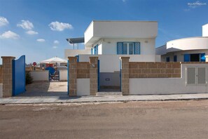 A modern building with a gated entrance, a covered outdoor seating area, and a clear blue sky. - 313 Appartamento Vicino Alle Spiagge di Pescoluse (Salve)