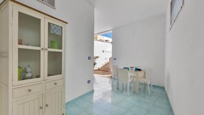 A narrow hallway with a white cabinet, a dining table with chairs, and a view of a staircase leading outside.
