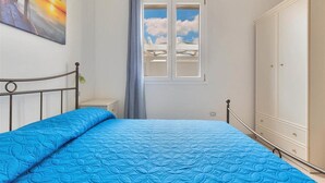 A bedroom with a bed, a wardrobe, a window with a view of a balcony, and a painting on the wall. - 1064 PMR - Appartamento Dei Delfini (Porto Cesareo)