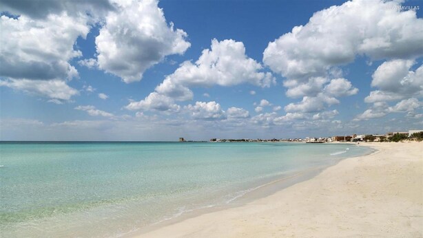 A beach with clear turquoise water, a sandy shore, and a distant town. - 1064 PMR - Appartamento Dei Delfini (Porto Cesareo)