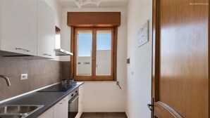 Eine kleine Küche mit weißen Schränken, einer schwarzen Arbeitsplatte und einem Fenster mit Holzjalousien.