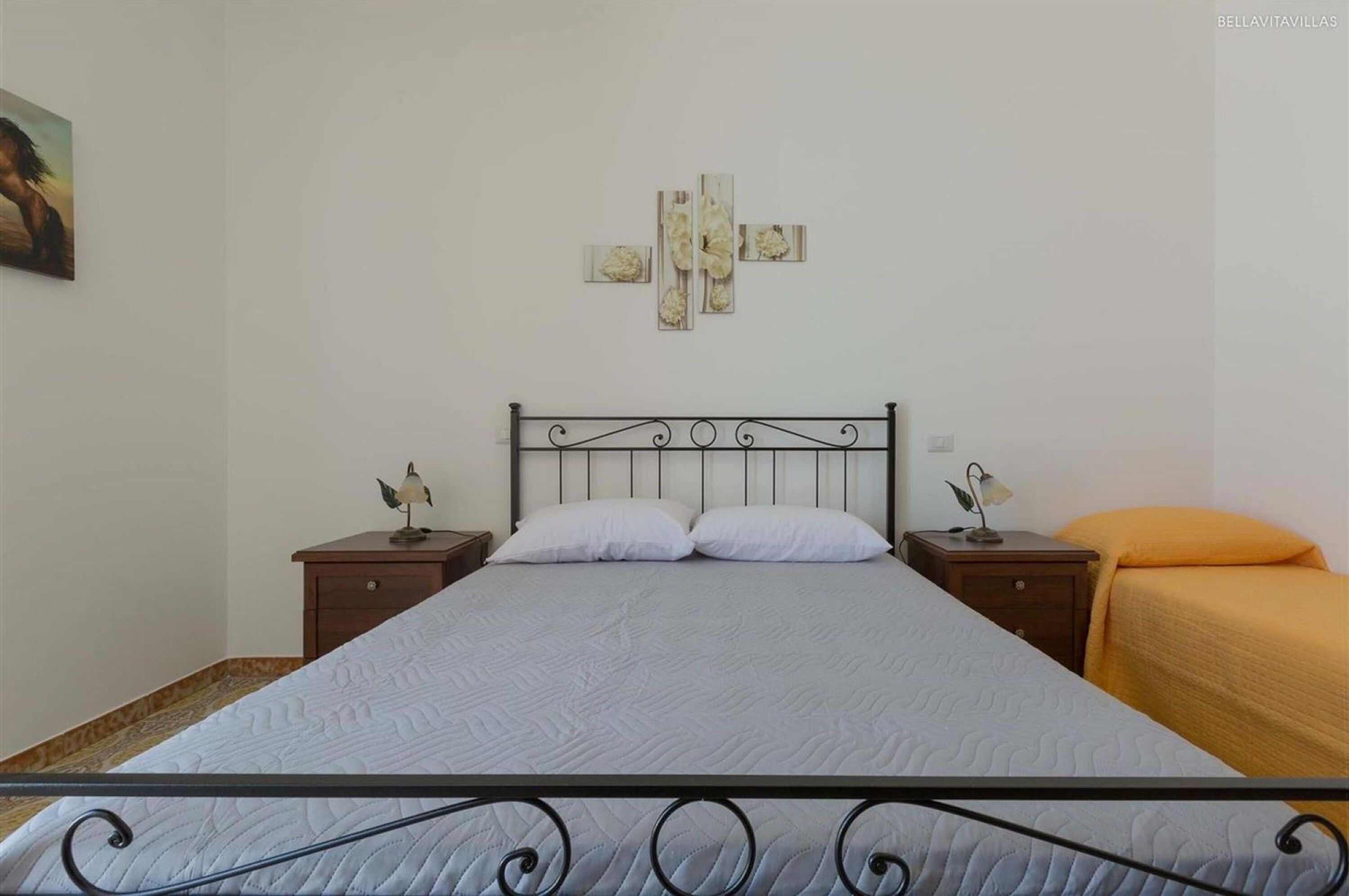 A single bed with a metal frame, two bedside tables with lamps, and a wall-mounted artwork.
