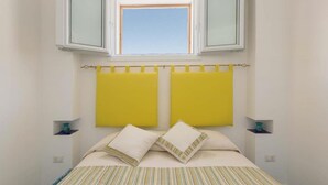 Un dormitorio con una cama, dos cabeceros amarillos, un ventanal y dos mesitas de noche decoradas.