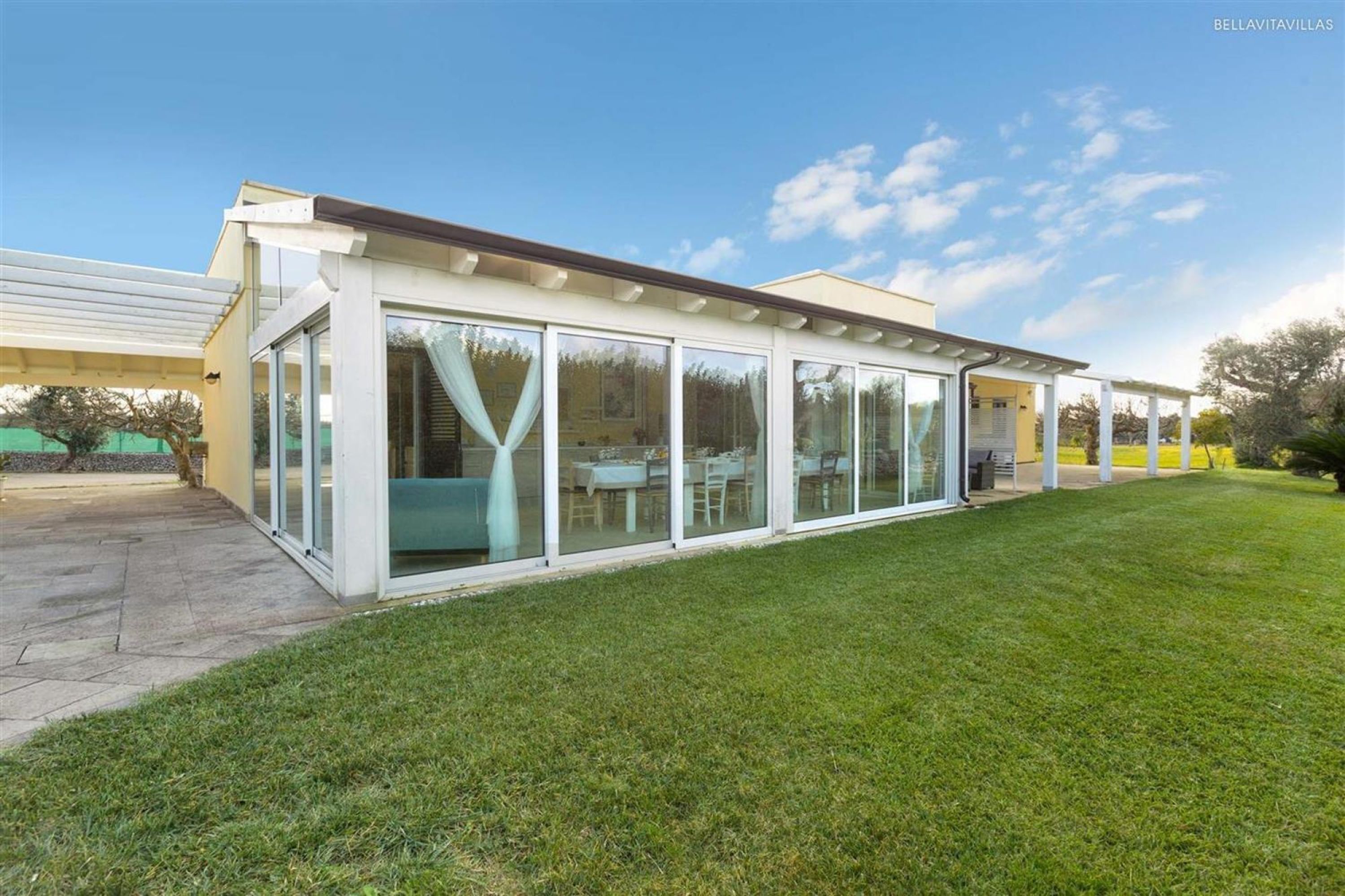 A modern house with large glass windows, a covered patio, and a well-maintained lawn.