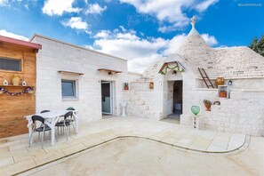 A courtyard with a white stone building, a wooden structure, and a table with chairs. - 1791 B B Mariano - Camera Tripla (Ceglie Messapica)