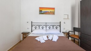 Un lit bien fait, avec des draps blancs, une couverture marron et un tableau représentant un coucher de soleil accroché au mur.
