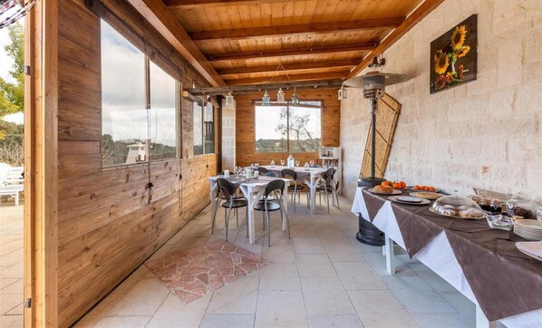 A wooden dining area with tables set for a meal, a stone-tiled floor, and a view through large windows. - 1791 B B Mariano - Camera Tripla (Ceglie Messapica)