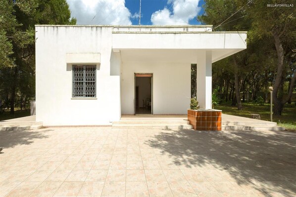 A modern white building with a covered entrance and a tiled patio. - 1975 Villetta La Pineta 2 by Barbarhouse (Porto Cesareo)