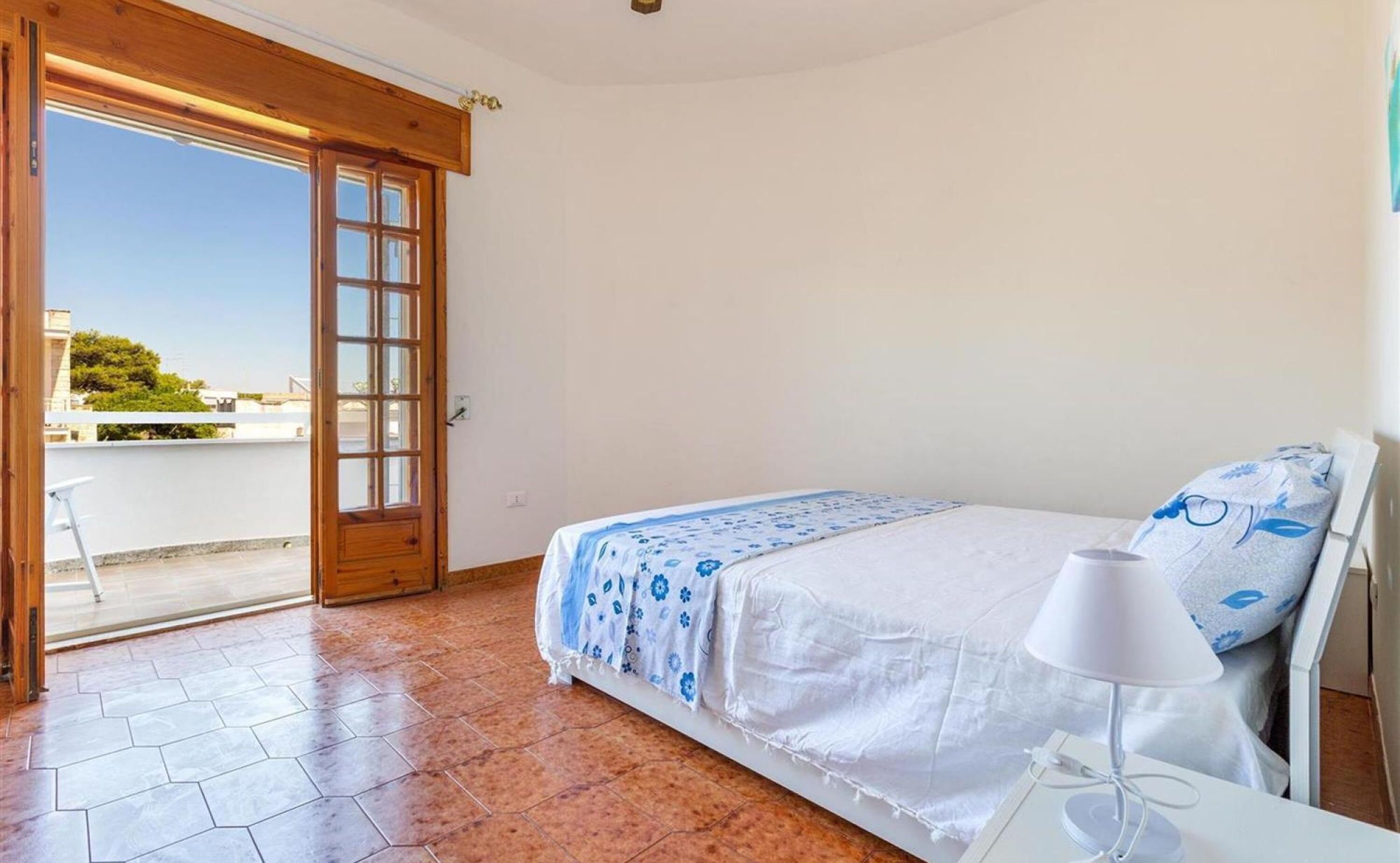A bedroom with a bed, a nightstand, a lamp, and a sliding glass door leading to an outdoor terrace.