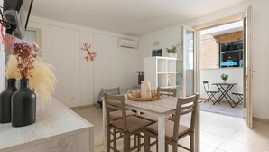 A modern kitchen with white cabinetry, a dining table with chairs, and a view of the street through an open door. - 2199 Al Castello Home Holidays - Mono by Barbarhouse (Otranto)