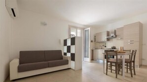 A modern living room with a sofa and a dining area with a table and chairs. - 2199 Al Castello Home Holidays - Mono by Barbarhouse (Otranto)