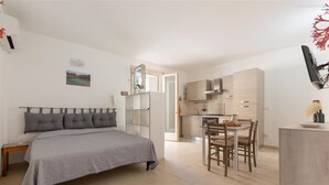 A bedroom with a bed, bedside table, and a view of the kitchen. - 2199 Al Castello Home Holidays - Mono by Barbarhouse (Otranto)