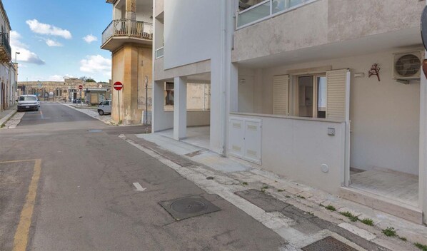 A street view with a building featuring a balcony, a stop sign, and a parked car. - 2199 Al Castello Home Holidays - Mono by Barbarhouse (Otranto)