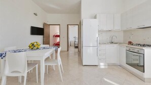 Eine moderne Küche mit weißen Schränken, einem eingebauten Backofen und einem Kühlschrank. Es gibt einen Essbereich mit Tisch und Stühlen sowie einen an der Wand montierten Fernseher.