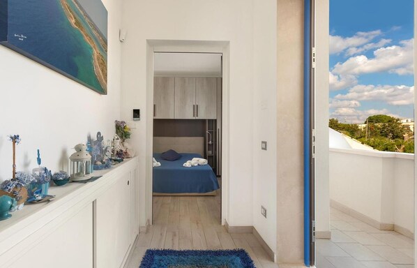 Un couloir étroit mène à une chambre à coucher qui contient un lit, une petite armoire et offre une vue sur le ciel.