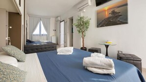 A hotel room with a bed, a TV, a plant, and a painting of a sunset.