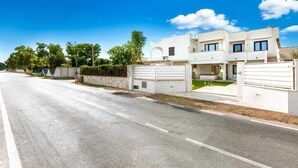 A modern two-story residential building with a gated entrance, a well-maintained lawn, and a clear sky.