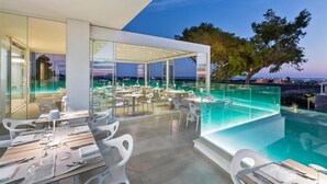 A modern outdoor dining area with tables and chairs, a glass enclosure, and a pool.