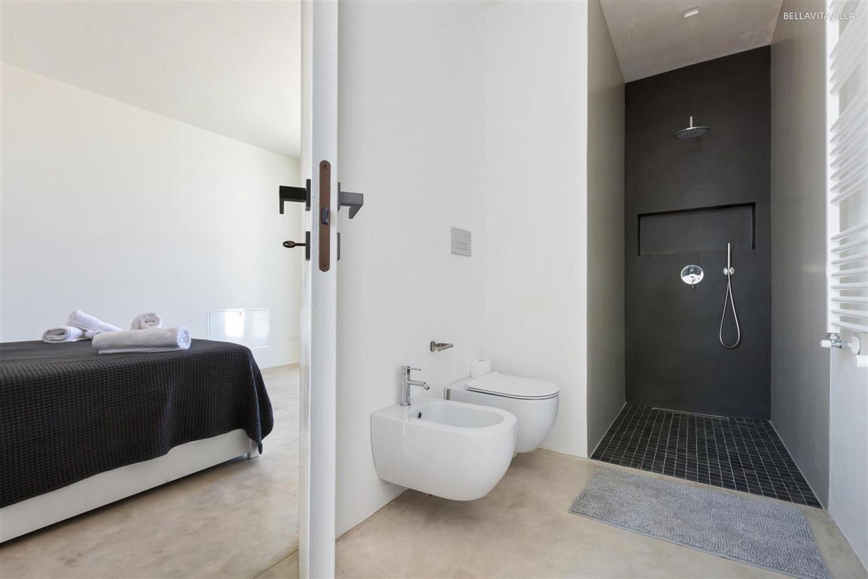A modern bedroom with a bed, a bedside table, and a bathroom with a shower, toilet, and bidet.