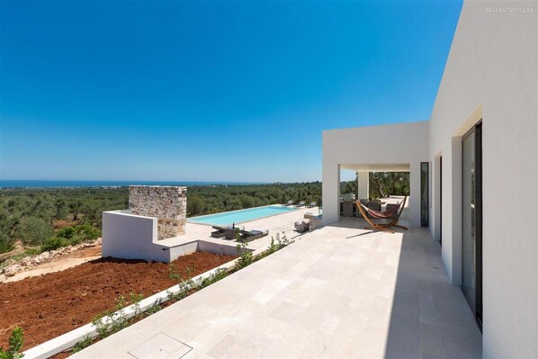 A modern villa with a pool, outdoor seating, and a view of the landscape.