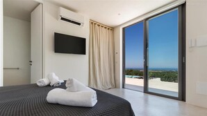 Ein modernes Hotelzimmer mit einem großen Bett, einem Flachbildfernseher, einer Schiebeglastür nach draußen und Blick auf die Landschaft.