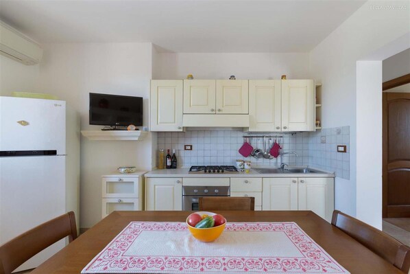 A compact kitchen with white cabinets, a gas stove, a sink, and a dining table with a placemat. - 1679 Villa Mila in Torre Vado (Morciano di Leuca)