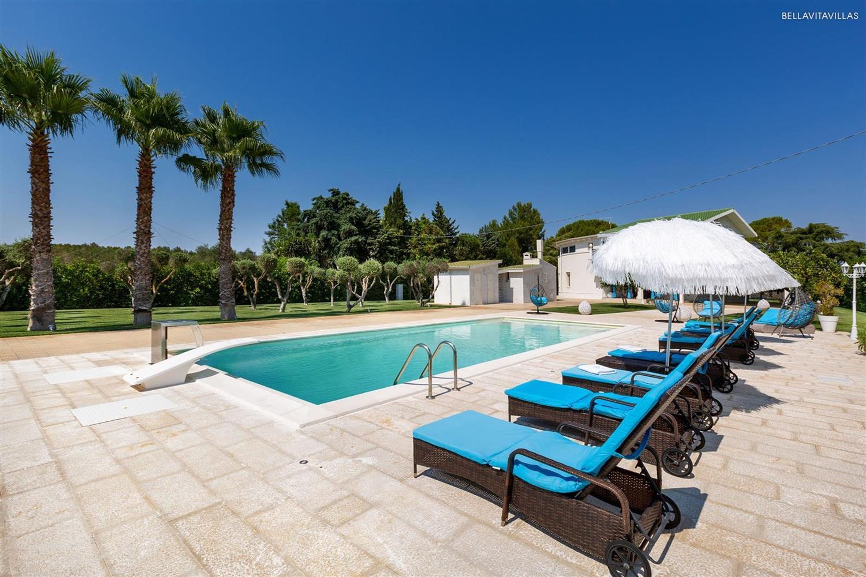 Zona piscina con sedie a sdraio e ombrellone di paglia.