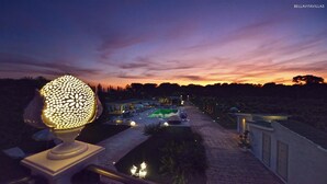 Een nachtzicht van een resort, met een pad dat leidt naar een zwembad, omringd door verlichte gebouwen en een decoratieve bolvormige lamp.